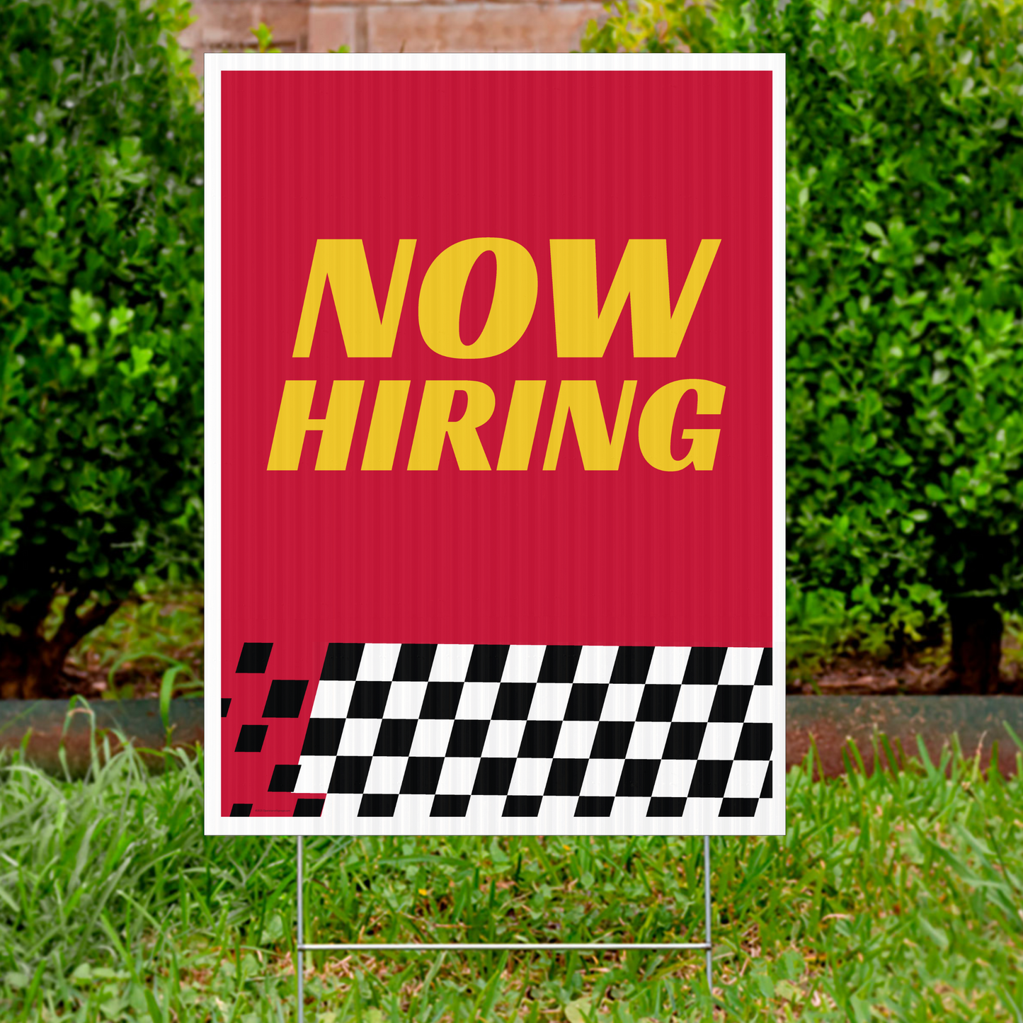 Red 'NOW HIRING' sign with a checkered pattern on a grassy background