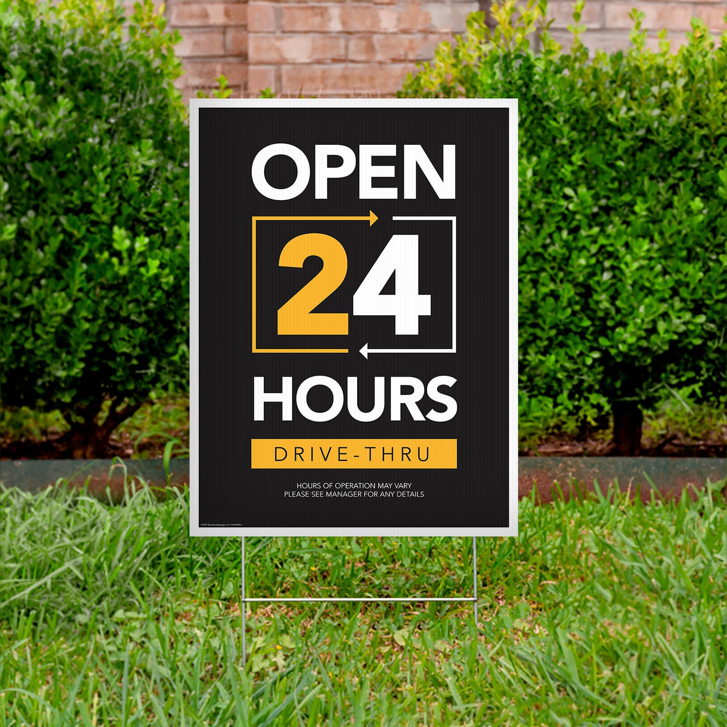 black, yellow, and white drive thru open 24 hours lawn sign in grass with bushes