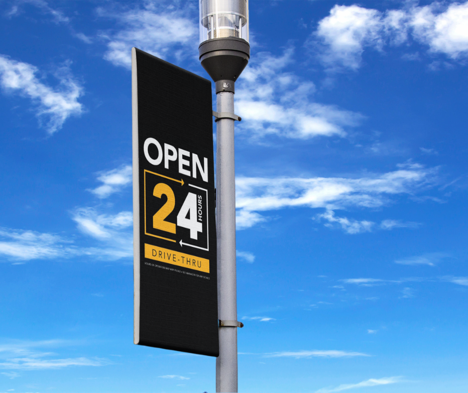 black white and yellow 24 hour drive thru banner on light pole blue sky background