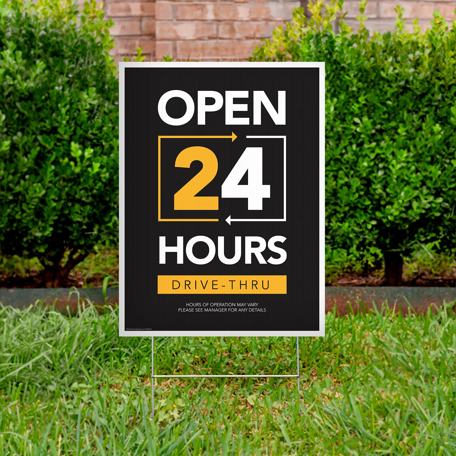 black, yellow, and white drive thru open 24 hours lawn sign in grass with bushes