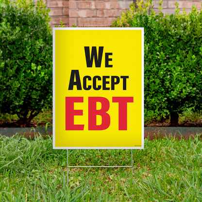 Yellow sign with 'We Accept EBT' text on a grassy lawn.