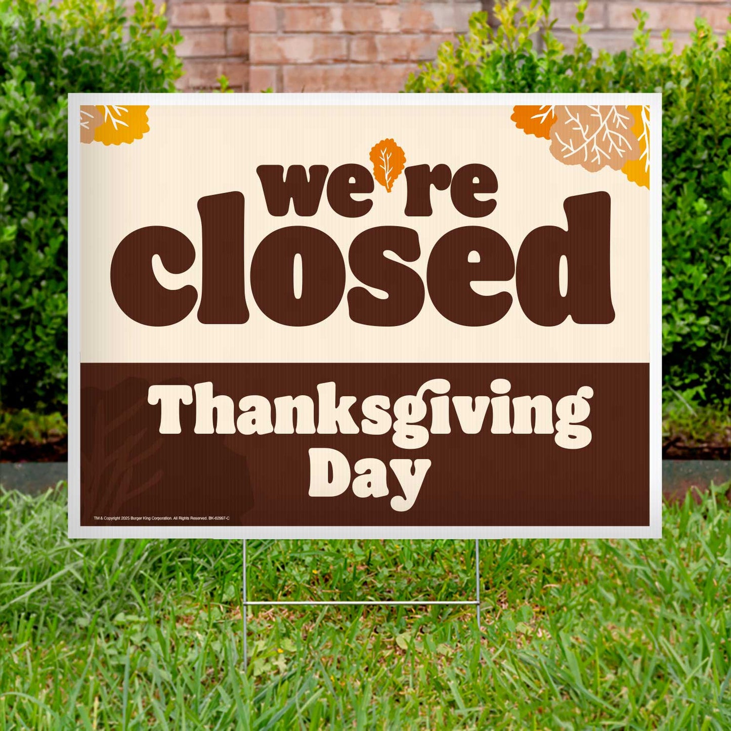 Closed sign for Thanksgiving Day on a grassy lawn with a brick wall and bushes in the background.