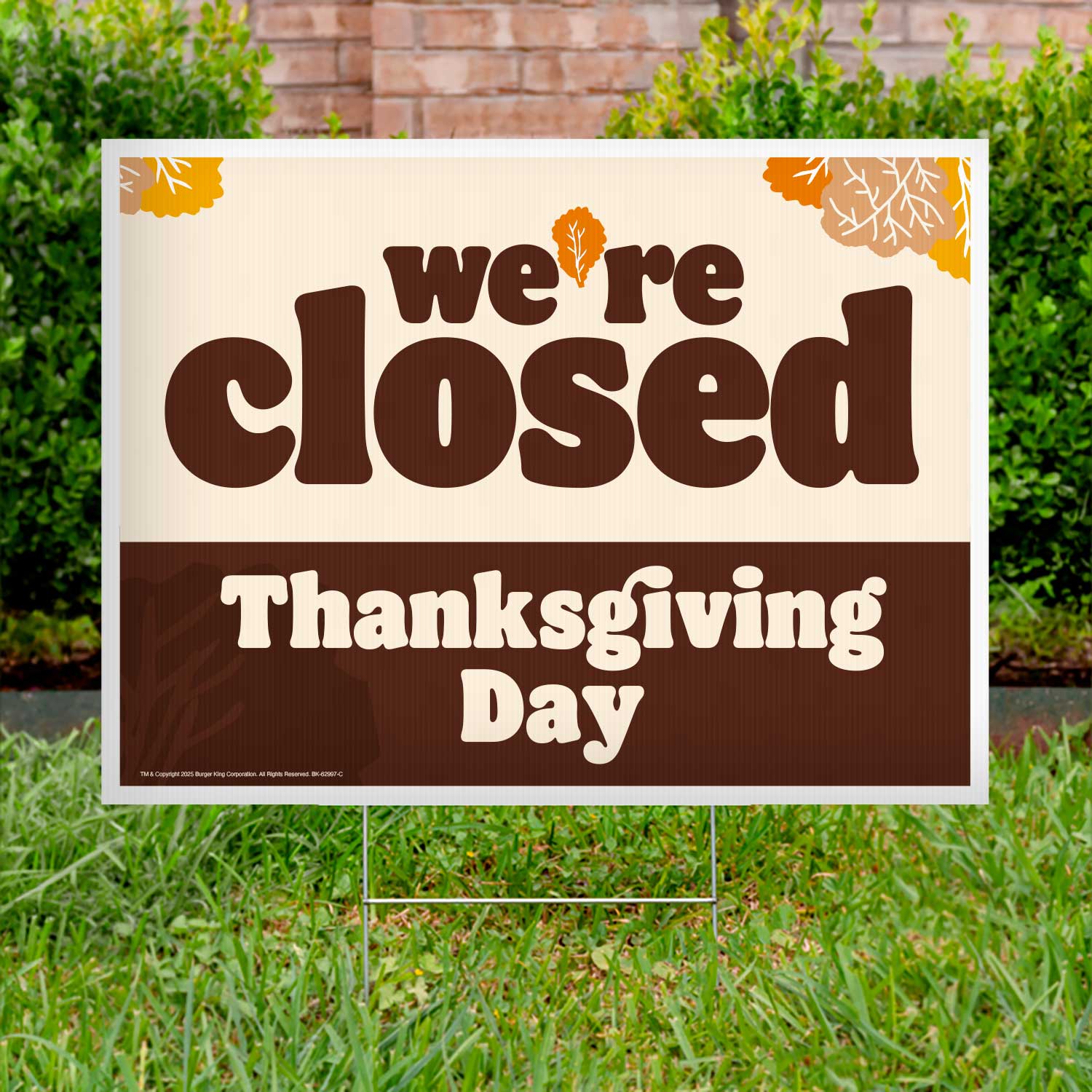 Closed sign for Thanksgiving Day on a grassy lawn with a brick wall and bushes in the background.