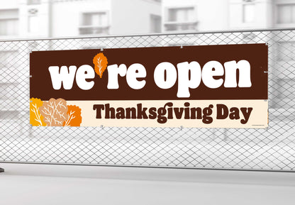 Banner on a fence stating 'we're open Thanksgiving Day' with autumn leaf designs.